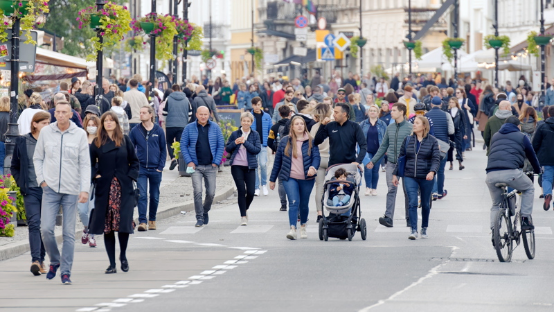 A bustling crowd of tourists walking down a street decorated with hanging floral baskets